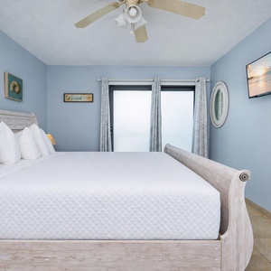 The master bedroom features a cozy white bed, a wall-mounted TV, and serene blue walls, creating a relaxing retreat