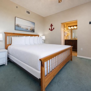 This inviting master bedroom features a king bed, soft green carpet, and an en-suite bathroom visible through an archway