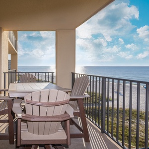 A spacious balcony features a dining table and chairs, offering a beautiful view of the beach and serene blue waters