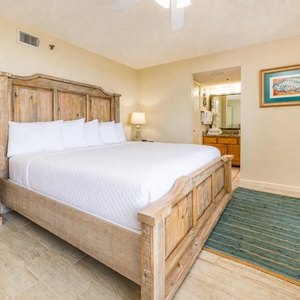 Master bedroom featuring a large king bed, wicker furniture, and a TV, with an en-suite bathroom visible in the background