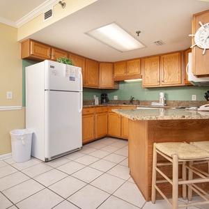 The kitchen features wooden cabinetry, white appliances, and a granite-topped island with two woven stools