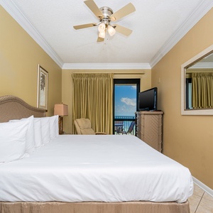 Inviting master bedroom features a king bed, a cozy armchair, and a view of the balcony with glimpses of the gulf beyond