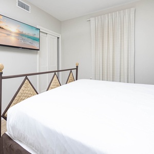Relax in this inviting guest bedroom featuring a stylish queen bed, a wall-mounted TV, and soft natural light