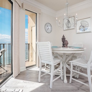 Bright dining area featuring a round table with white chairs, offering a stunning view of the beach from large glass doors