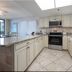 The kitchen features stainless appliances, granite countertops, coffee maker, and a beautiful beach view from the dining area