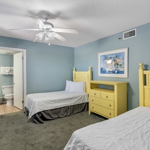 Guest bedroom features two twin beds with bright yellow headboards, a cheerful dresser, and an en-suite bathroom