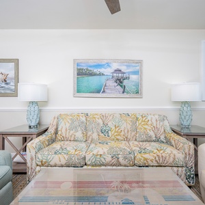 The living area features a floral-patterned sofa, light blue armchair, and coastal art, creating a relaxed beach vibe