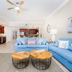 Inviting living area with comfortable blue seating, decorative accents, and a view into the stylish kitchen area