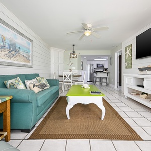 Living area features a turquoise sofa with colorful pillows, a unique green coffee table, and a view toward the dining space