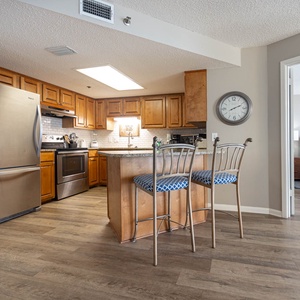 Kitchen features warm wood cabinetry, a breakfast bar with stylish seating, and a view into the inviting bedroom