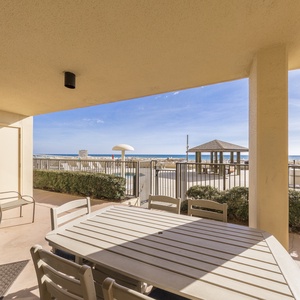 A spacious outdoor beach patio features a dining table and chairs, offering a view of the beach and nearby pool area