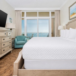 Relax in the inviting master suite featuring a king bed, a cozy chair, and stunning beach balcony views