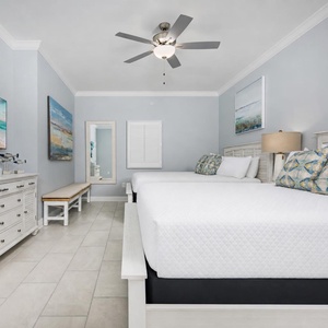 Cozy guest bedroom featuring two queen beds, decorative pillows, and coastal artwork for a relaxing retreat