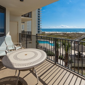 Balcony seating offers a serene view of the beach and pool area, perfect for relaxing under the sunny sky