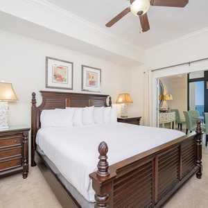 Elegant master bedroom featuring a king-size bed, warm lighting, and a view of the inviting dining area and balcony beyond