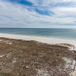 Expansive view of the tranquil gulf waters and white sand beach, framed by lush coastal vegetation and a wooden walkway
