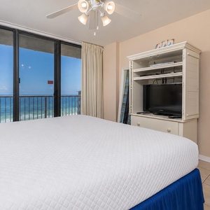 The master bedroom features a comfortable bed, a TV, and stunning beachfront views through large glass doors