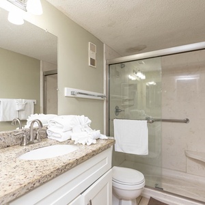 The bathroom features a stylish granite countertop, a spacious glass shower, and neatly arranged fresh towels