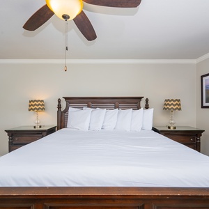 The inviting master bedroom features a king bed with crisp white linens, stylish lamps, and a serene beach-themed artwork