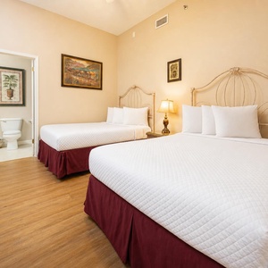Bright guest room featuring two double beds with elegant headboards, warm wood flooring, and tasteful art enhancing the decor