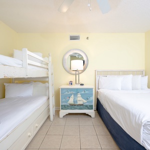 Brightly decorated guest bedroom featuring a queen bed, twin bunk beds, and a charming dresser with nautical artwork