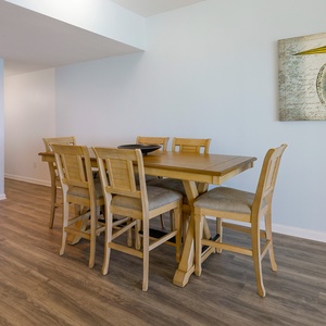 Dining area featuring a wooden table with eight chairs, complemented by coastal artwork on the wall
