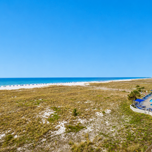 Stunning view of the beach with emerald waters and white sand, framed by lush greenery and a sparkling pool area nearby