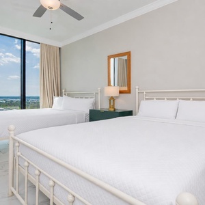 Rest in this guest bedroom featuring two queen beds, soft bedding, and large windows offering beach views
