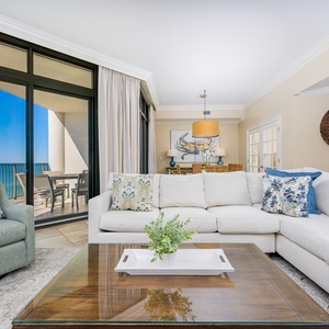 This living area features a plush sectional sofa, vibrant pillows, and a stunning beachfront view from the large glass doors