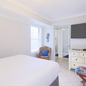 The bedroom features a cozy chair by the window, a large TV, and a stylish dresser, perfect for relaxation