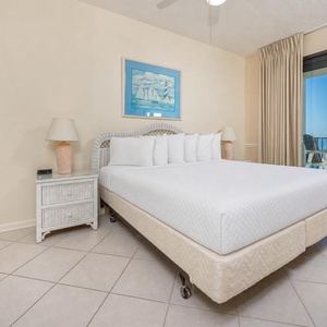 Master suite featuring a large king bed, coastal decor, and a balcony with seating overlooking the beach