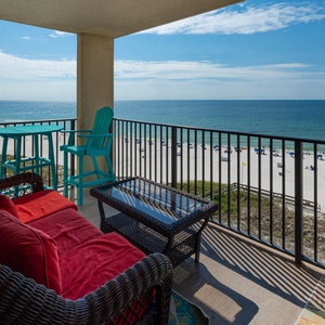 The balcony features a cozy seating area with red cushions and turquoise bar stools, offering a breathtaking beach view