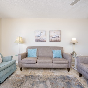 The cozy living area features a comfortable sofa with decorative pillows, accent chairs, and charming bird artwork