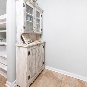 This cozy nook features a charming white bunk bed and a rustic cabinet, perfect for kids and family gatherings