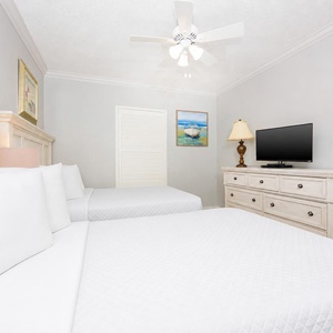 Rest in this comfortable guest bedroom featuring two double beds, a TV, and soft lighting for a relaxing stay