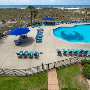 Pool area features vibrant lounge chairs and umbrellas, with a scenic view of the beach just beyond the grassy dunes