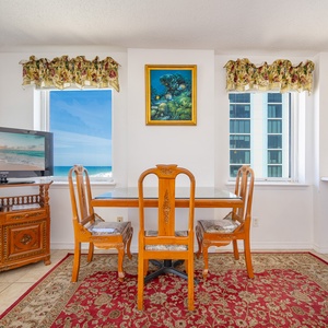 This inviting dining area features a wooden table, a TV, and a lovely view of the beachfront through sliding glass doors