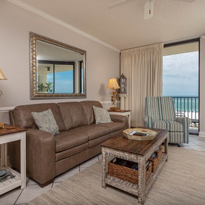 Living area features a brown leather sofa, striped chair, and a stunning view of the beach through large windows