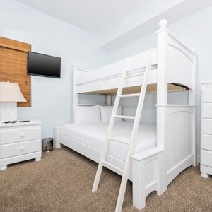 This guest room features a white bunk bed, a flat-screen TV, and a warm atmosphere perfect for family stays