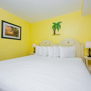 This inviting bedroom features a large bed with plush pillows, bright yellow walls, and tropical decor for a cheerful vibe