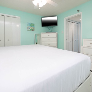 Guest bedroom features a large king bed, a colorful lamp, a mounted TV, and soft aqua walls, creating a tranquil vibe