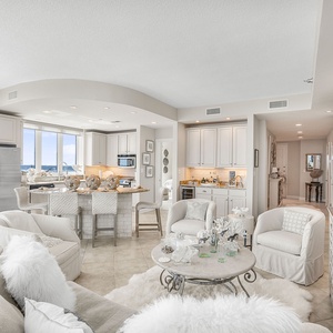 The living space features a sleek kitchen with stainless appliances, a cozy seating arrangement, and a stunning beach view