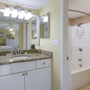 Master bathroom featuring a granite countertop, a tub/shower combo, and a mirror reflecting the adjacent bedroom