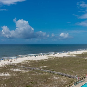 Expansive view of the beach with white sand, beach chairs, and a sparkling pool area, perfect for relaxation and fun