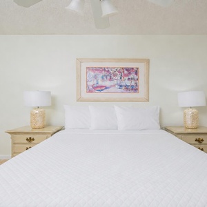 Soothing guest bedroom featuring a large queen bed complemented by decorative lamps and vibrant artwork