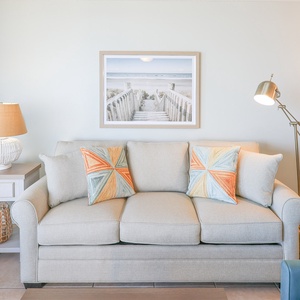 Unwind on the soft sofa adorned with colorful pillows, complemented by a stylish lamp and beach artwork