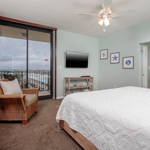 Cozy master bedroom features a king bed, a wicker chair, and a TV, with sliding doors leading to a balcony