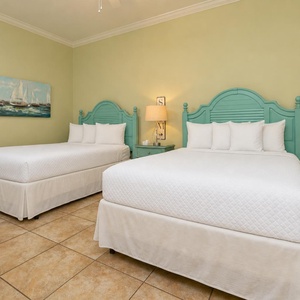 This guest bedroom features two queen beds with turquoise headboards, soft white linens, and a serene sailing-themed artwork