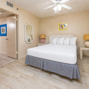 Bright and airy guest bedroom featuring a plush queen bed, soft lighting from two lamps, and a decorative mirror