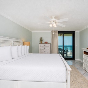 Stylish master suite bedroom features a king bed, a TV, and a balcony door offering a view of the beach beyond